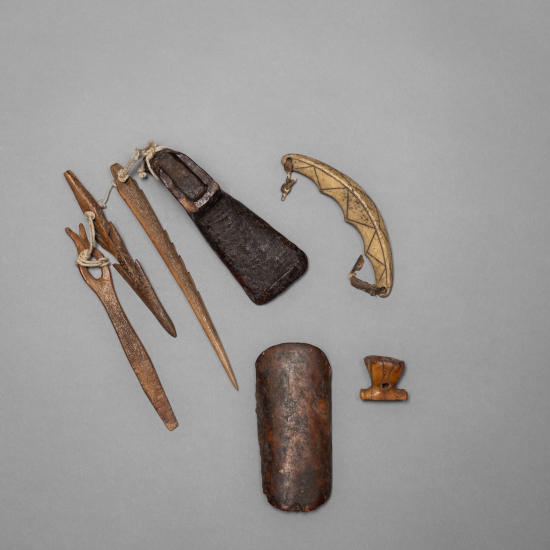 A group of seven Eskimo tools parts, with a bow guard: A group of seven Eskimo artifacts, comprising various, bone and wood tools along with a carved bow guard. The adze head with three attached components. Each showing distinct surface wear and