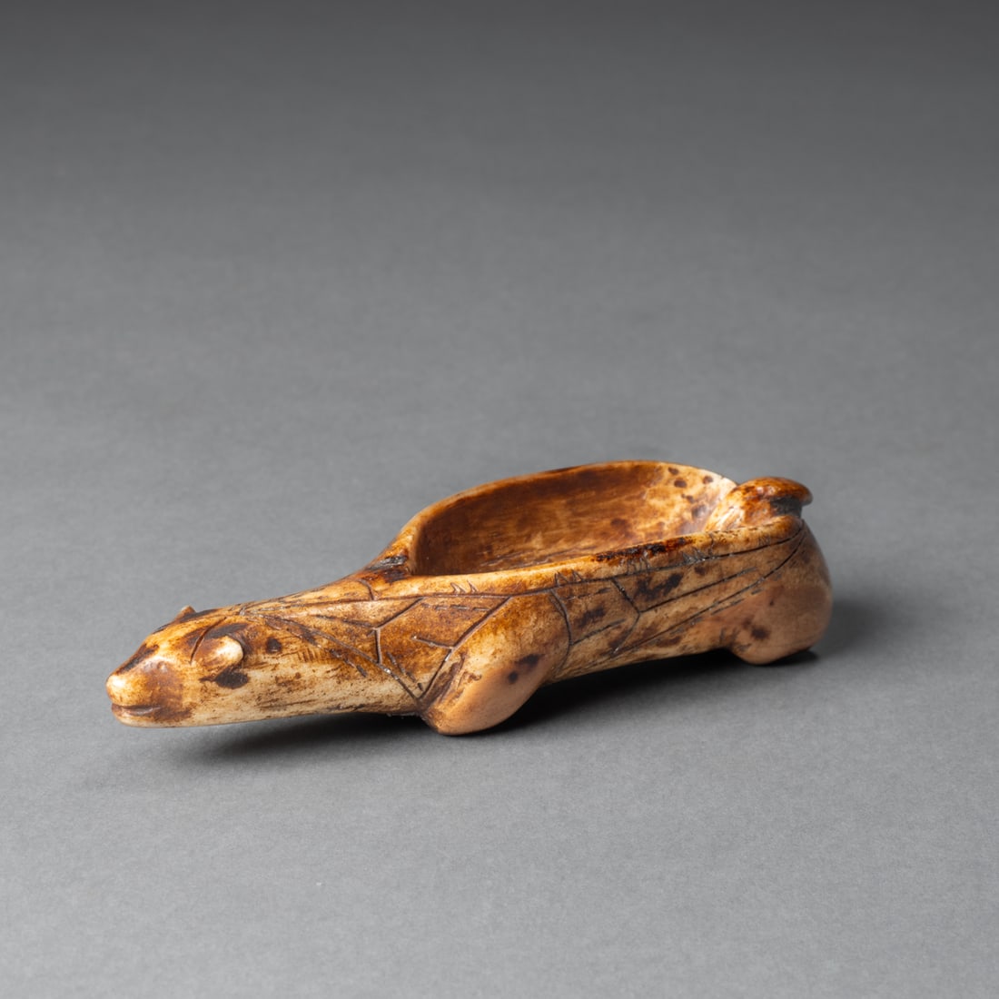 A Bering Sea Eskimo bear pigment bowl: Bering Sea Eskimo bowl in the form of a stylized bear, with a deep basin carved in the center, exhibiting a rich aged patina and incised line decoration. The head is finely modeled with subtle