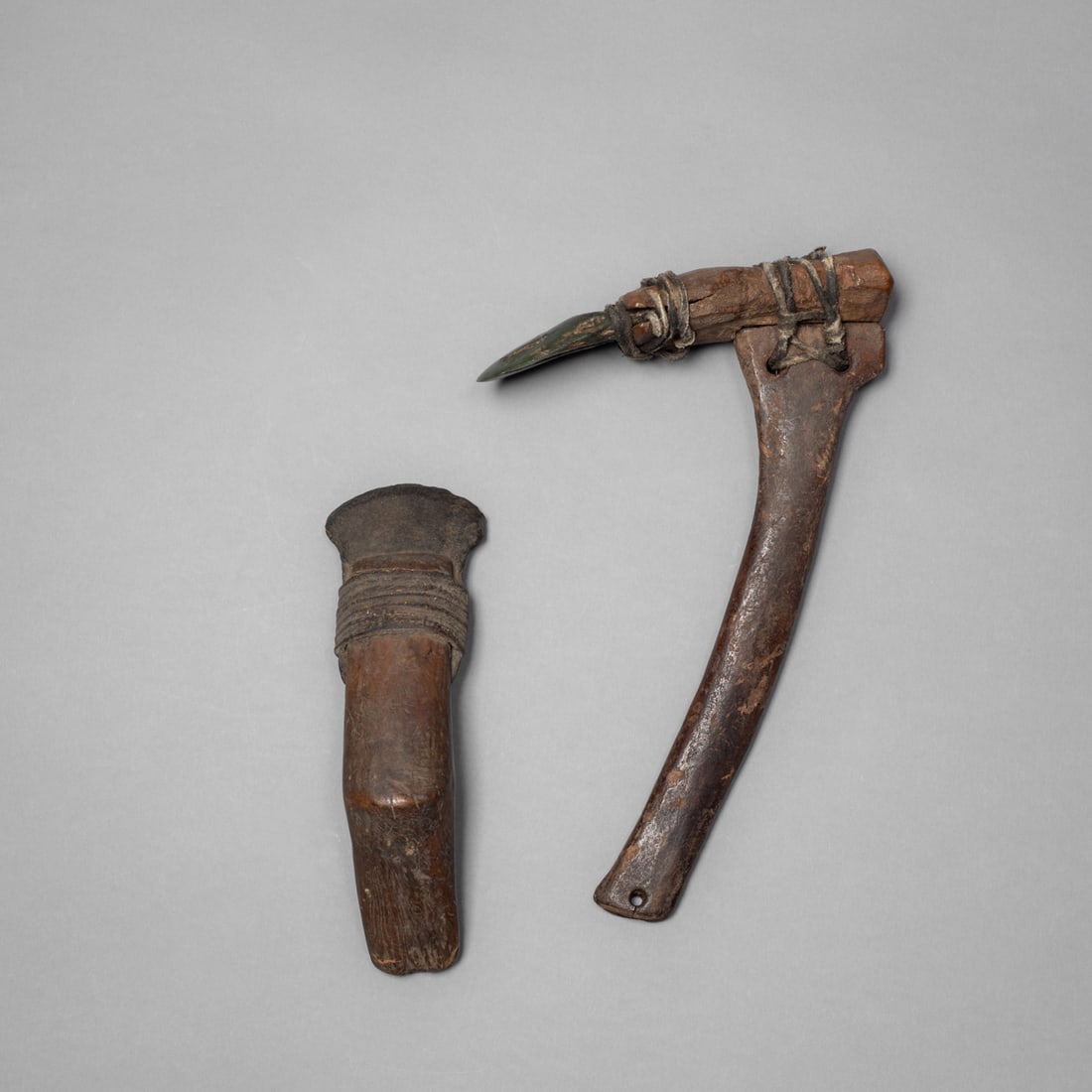 An Eskimo hafted adze and scraper: 19th century, a pair of traditional wood working tools, each with a stone blade lashed to a wooden handle using sinew and hide cord. The adze features a curved haft exhibiting a smooth patina from