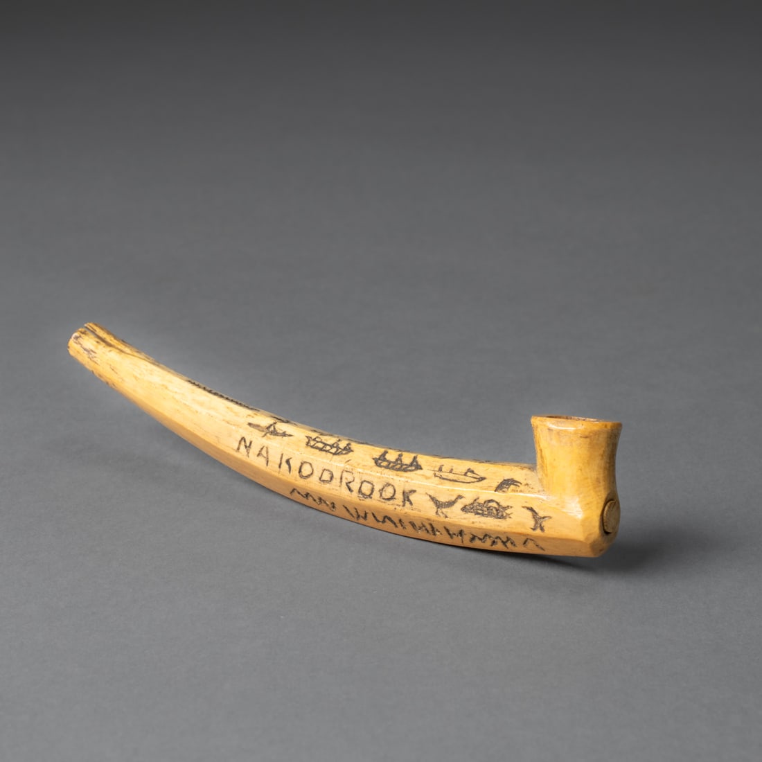 An Eskimo pipe: Alaska, late 19th/early 20th century, the pipe decorated with incised pictorial and syllabic decoration, including depictions of animals and the name “NAKOOROOK.” With a smooth patina from