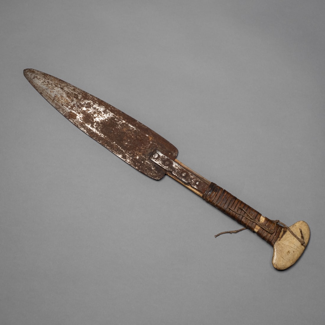 An Eskimo knife: Alaska, 19th century, the knife featuring an iron blade secured to a bone handle with tight hide wrapping. The broad blade exhibits a darkened, time-worn patina. The haft shows smooth wear from