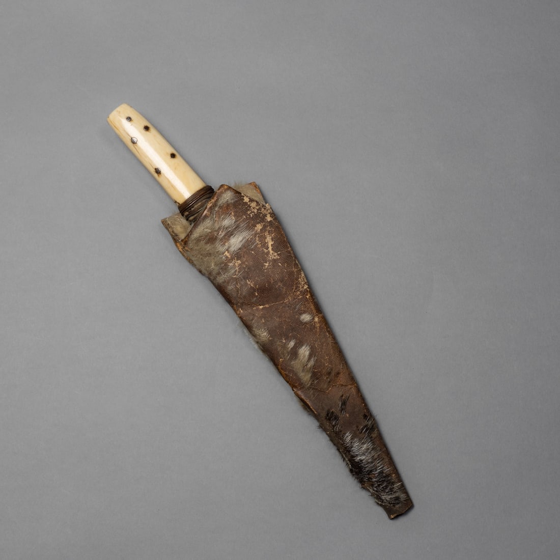An Eskimo knife and sheath: Alaska, 19th century, a traditional Eskimo knife featuring a forged iron blade secured to a carved handle with copper wire, accompanied by its original sealskin sheath. Knife lg. 11 ½, sheath l