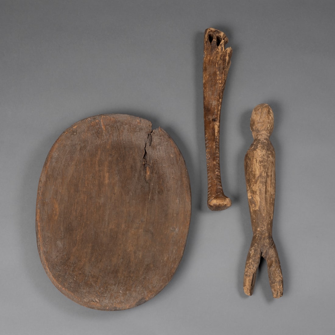 An Eskimo wood dish, adze handle and figure: Alaska, 19th century, a shallow wood food dish, a wood adze handle with blade missing and a large wood figure with carved facial features and short legs. 12 1/4 x 9 1/4, lg. 12 3/4 and lg. 12 1/2 in.
