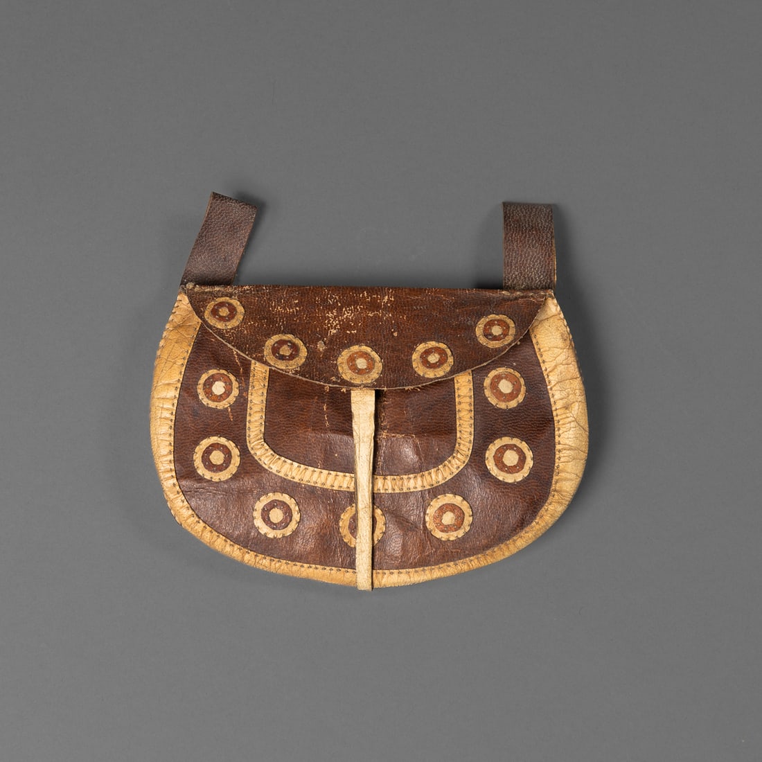 An Eskimo bag: Bering sea hunters/tool pouch, made of tanned seal skin and bleached deer hide with black dyed sinew. The circles are appliqued using the same black sinew. Ht. 4 ½, wd. 7 in. Provenance: The