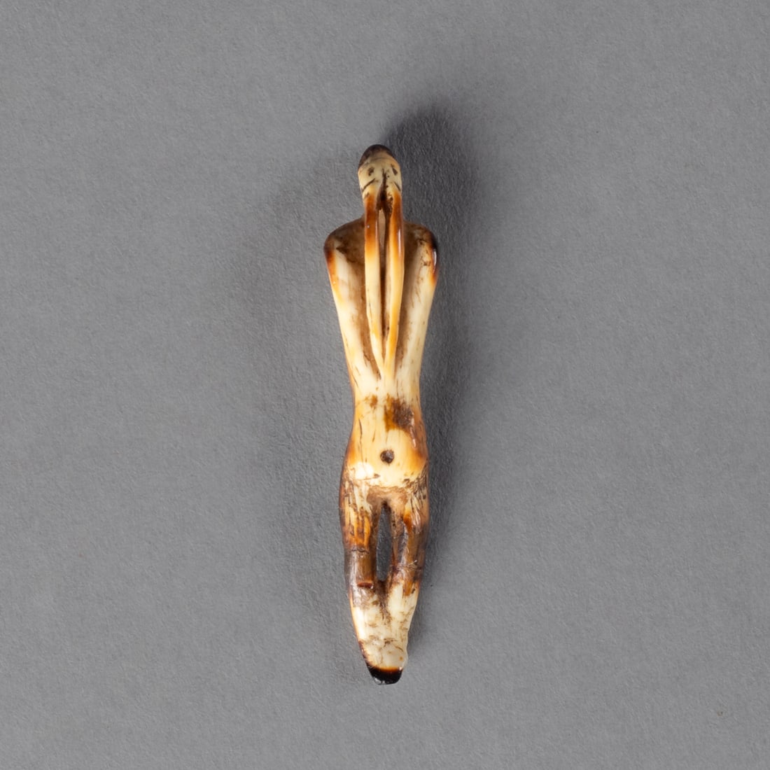 An Eskimo transformation figure: Alaska, 19th century, or earlier, the elongated human figure with cutout legs, arms incorporated into the torso, the head with two eyes and two long projecting tusks. Ht. 1 1/2 in.