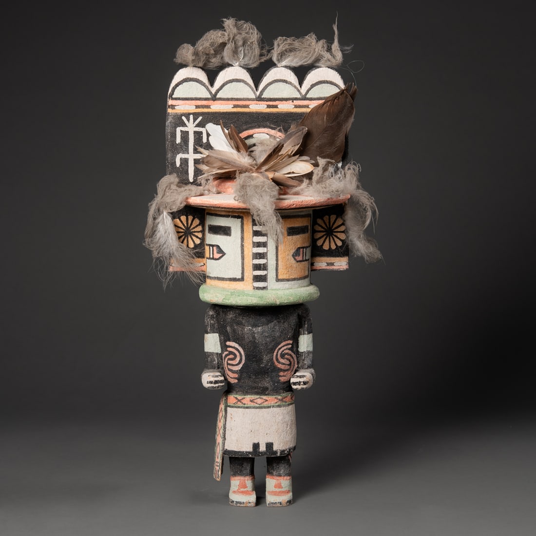 A Hopi Hemis katsina: Carved in traditional form with wide, elaborately painted tableta. The figure wears a black-painted body with spiral motifs, kilt with geometric design elements, and a headdress painted in orange,