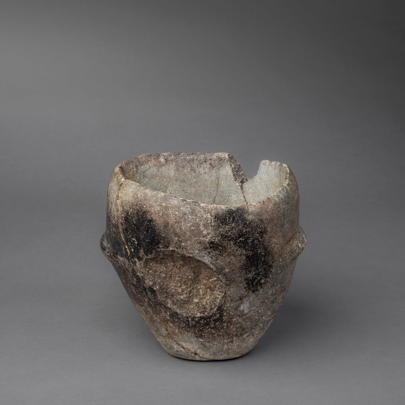 A Zuni stone silver crucible: The deep hollowed out stone with raised handles on each side, the exterior blacked in places, broken in two and restored, with stone missing from rim and sides. Ht. 7 1/2, wd. 7 in. Provenance: Larry