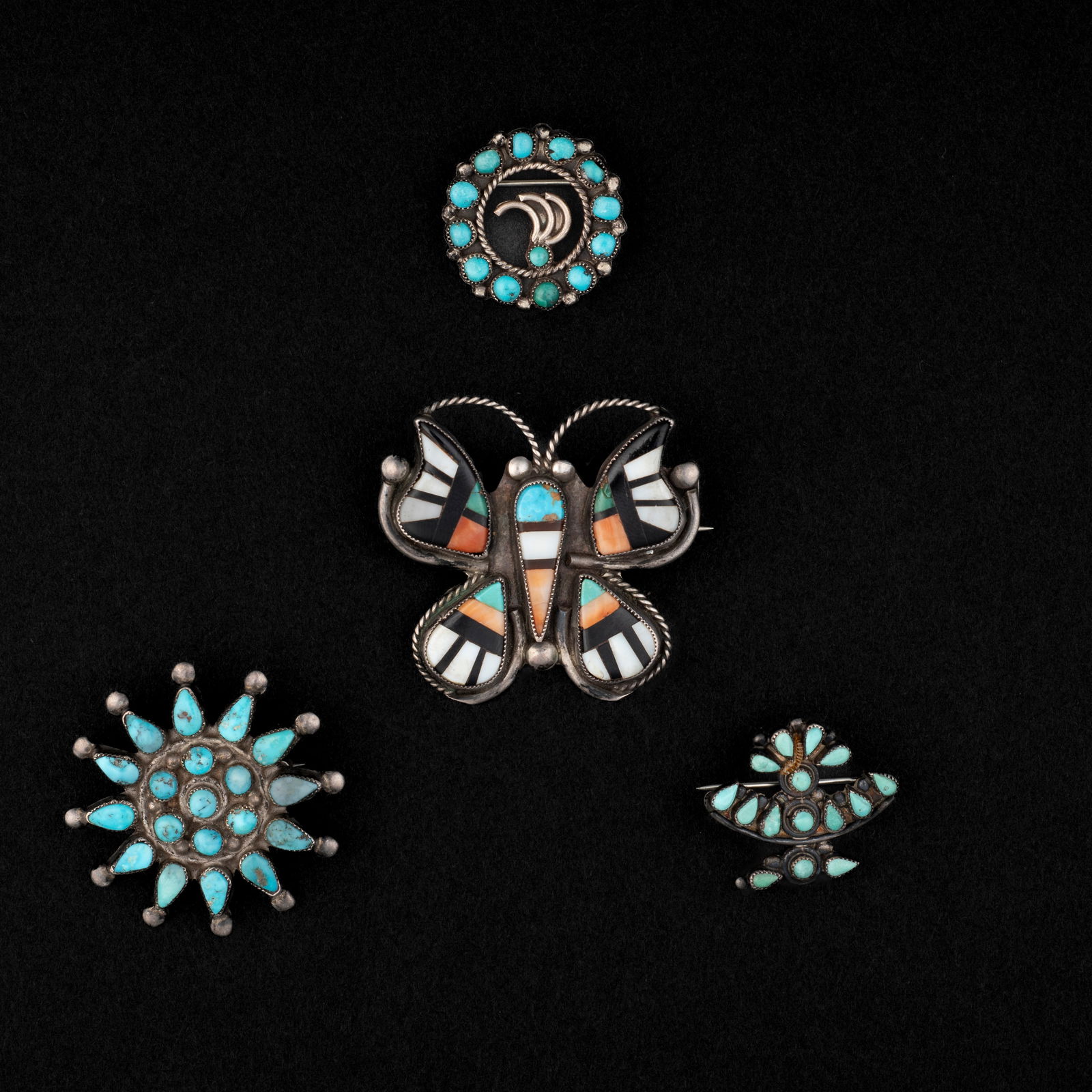 Four Zuni silver and turquoise pendants: An inlayed butterfly brooch with jet, turquoise, shell and spiny oyster, with three turquoise cluster brooches. 1 1/2 x 1 5/8, 1 1/2 x 1 1/2, dia. 1, and 1 x 1 in.