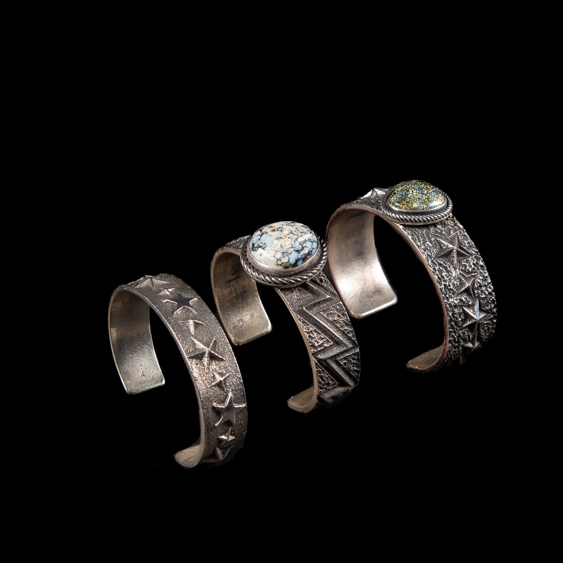 Three Kevin Yazzie tufa cast silver bracelets: Two bracelets with single turquoise/variscite setting surrounded by rope work, and a third tufa cast bracelet with stars, each marked "K' and "Sterling." Total interior circumference (including gap) 6