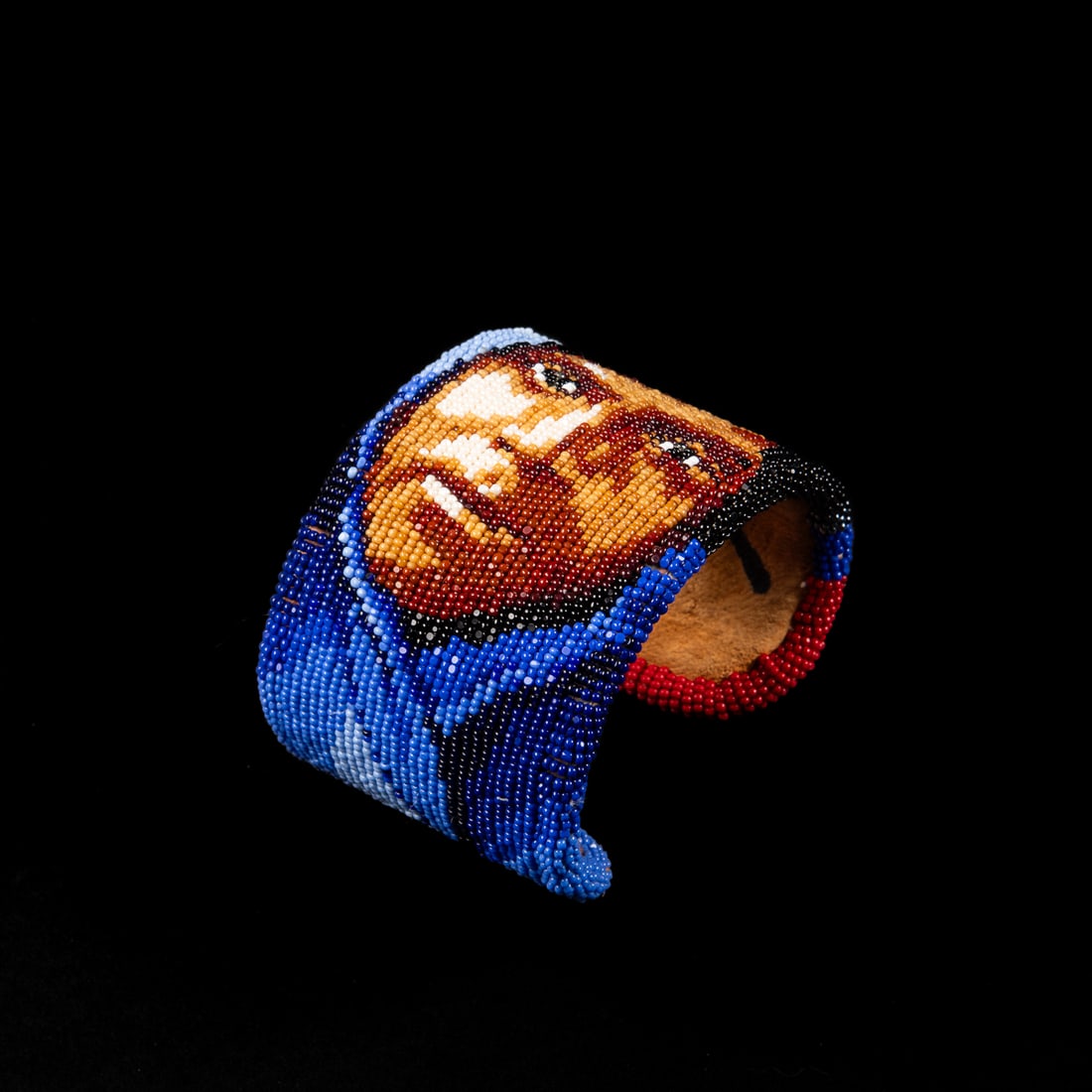 A Marcus Amerman cuff bracelet: Marcus Amerman, Choctaw (b. 1959), a leather beaded cuff with the face of a Native American, signed on the interior. Total interior circumference (including gap) 7 1/8, wd. 2 1/8, gap 1 in. Gross