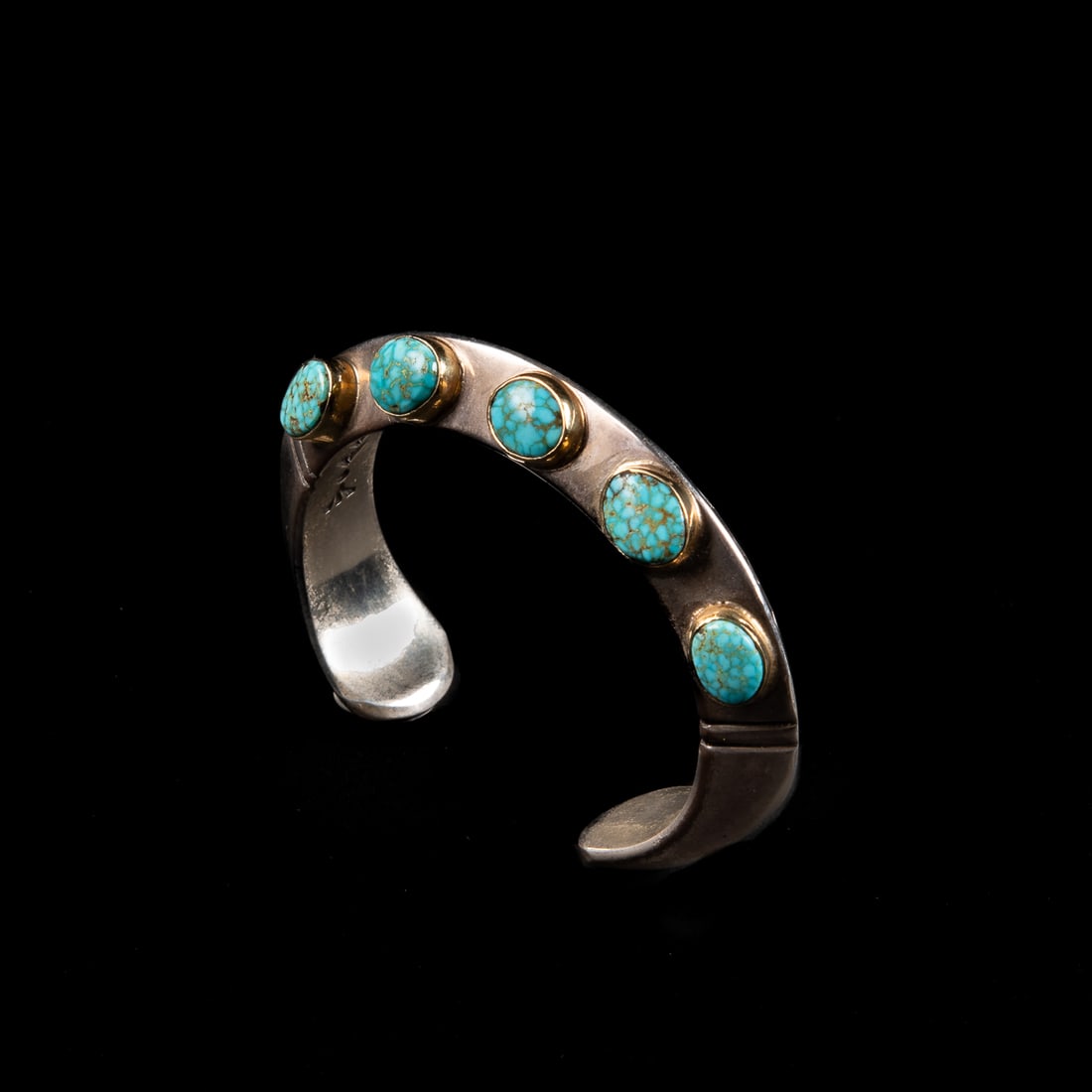 A Lyle Secatero silver and turquoise cuff bracelet: The heavy Sterling silver carinated cuff with a double wavy line design on one side and five turquoise settings on the other with gold bezels, signed "Lyle Secatero," and marked "18k" And "Sterling."