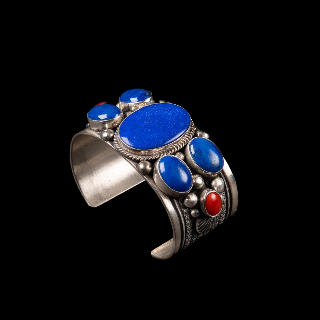A Guy Hoskie cuff bracelet: The wide Sterling silver cuff decorated with stamp, ball and ropework, with six lapis and two coral settings, marked "GH," and "Sterling." Total interior circumference (including gap) 6 1/2, wd. 1 1/4