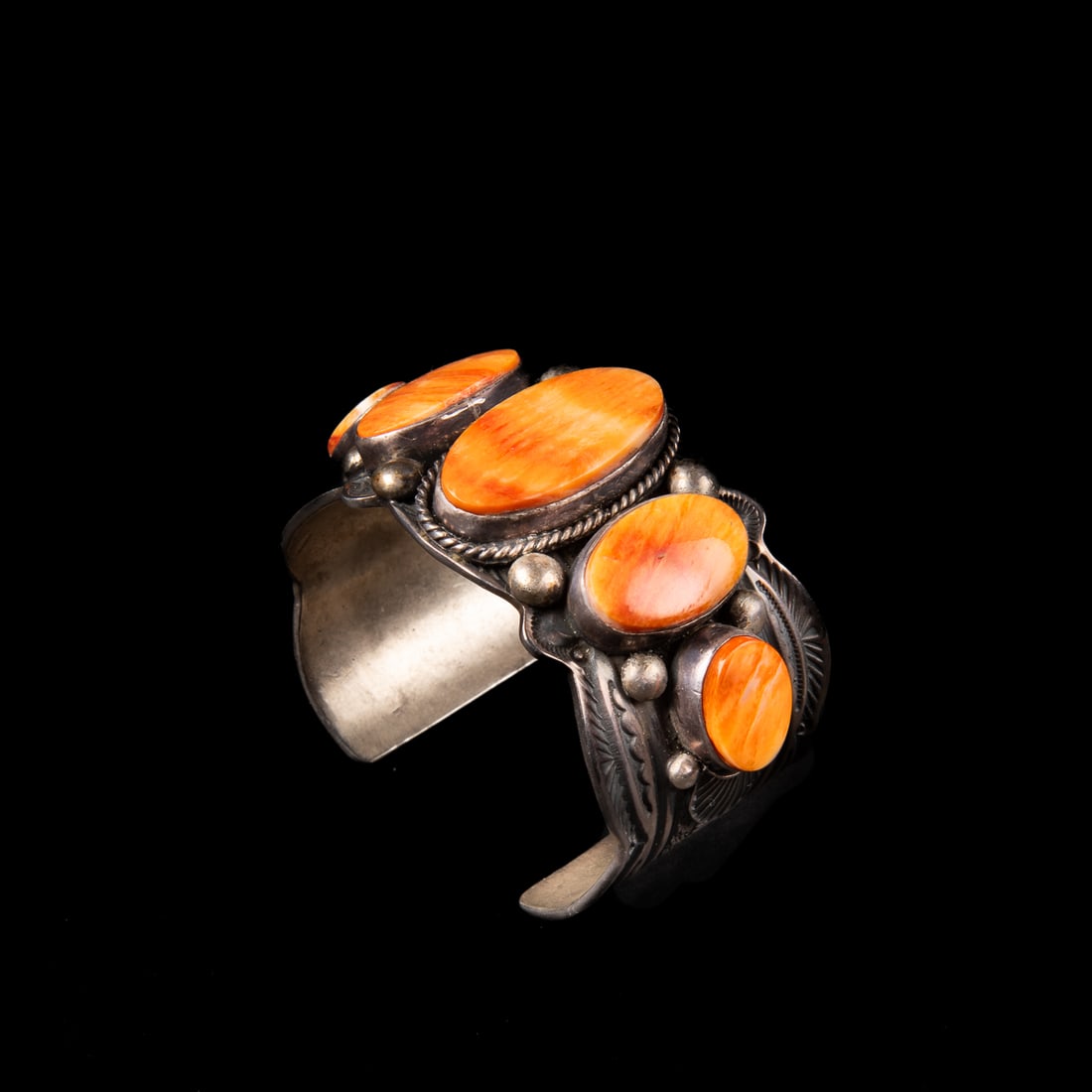 A Guy Hoskie cuff bracelet: The wide Sterling silver cuff decorated with stamp, ball and ropework, with five graduated spiny oyster settings, marked "GH," and "Sterling." Total interior circumference (including gap) 6 1/8, wd. 1