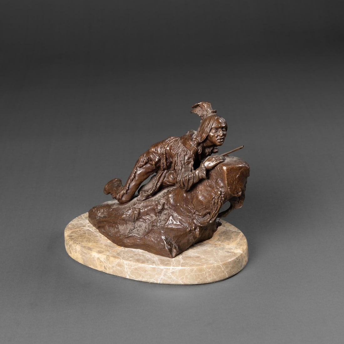 A Carl Kauba bronze sculpture: Carl Kauba (1865-1922), Austria. Circa 1910. The small bronze sculpture, depicting a Native man crouched low over a rocky ledge, holding a rifle and gazing into the distance. Cast in dark brown