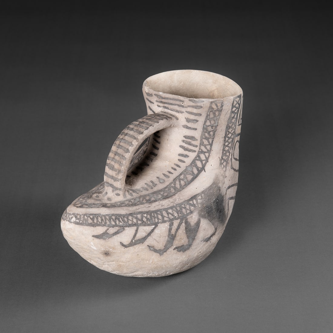 An Anasazi black-on-white duck effigy pitcher: Circa 1150-1350 A.D., formed with a low rounded body and an arched strap handle rising to a short cylindrical neck, painted in mineral black on a light slipped ground, with geometric banding and styli