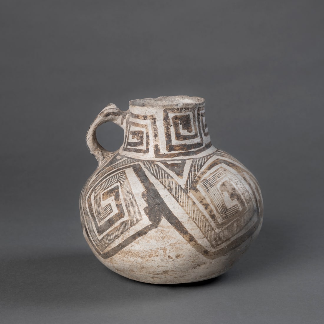 An Anasazi vessel with handle: Circa 1100 A.D., the bulbous vessel decorated all-over with dark brown geometric designs on a white ground, with tall neck and loop handle attached, (restoration to pigments in places). Ht. 7, wd. 6 1