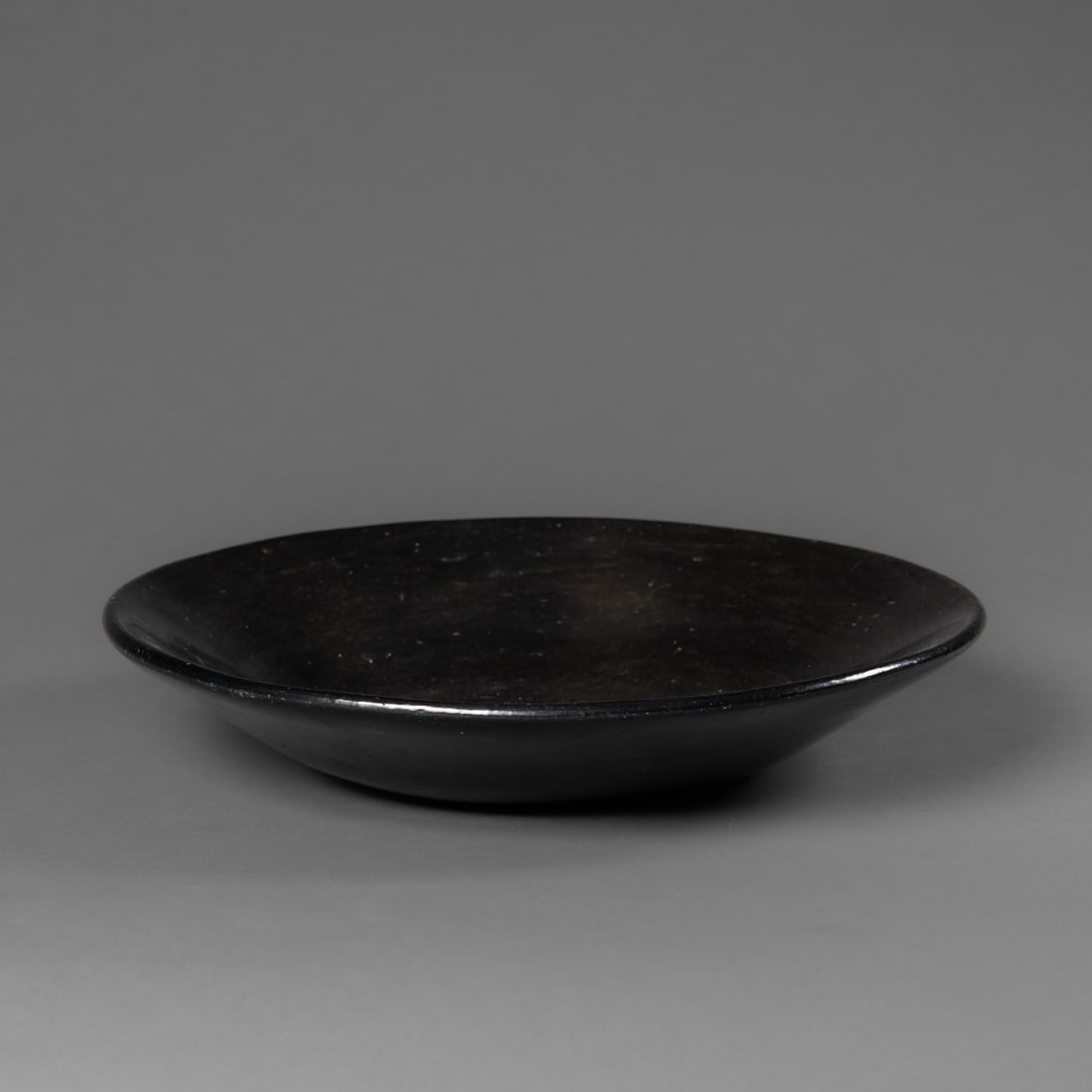 A Santa Clara blackware bowl: Late 19th/early 20th century blackware shallow bowl, attributed to Sara Fina, with a Fred Harvey label on the bottom. Ht. 2 1/2, dia. 11 1/2 in. Provenance: The James Pavitt and Carolyn Stettner colle