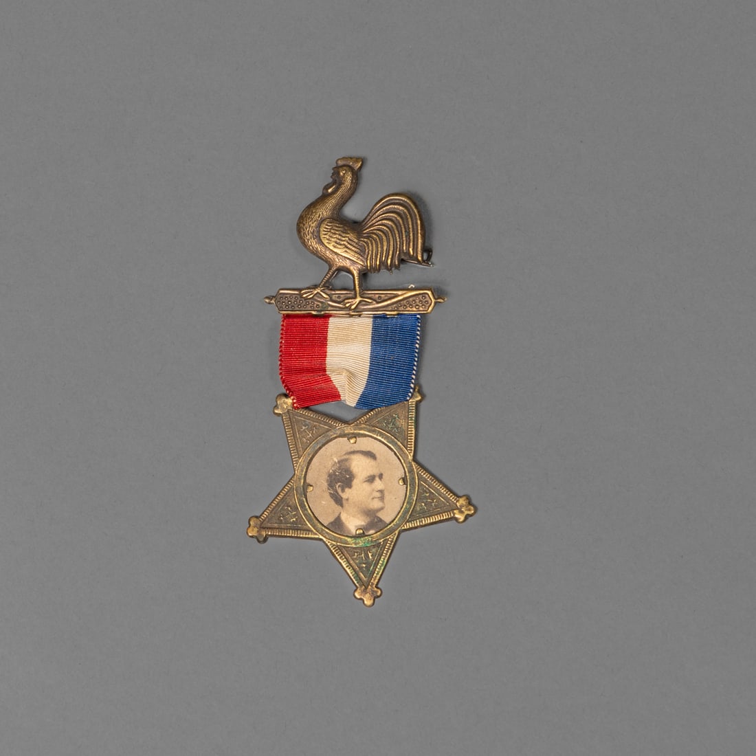 A 19th century William Jennings Bryan political campaign medal: 19th century political campaign medal featuring a brass rooster pin above a red, white, and blue ribbon, suspending a five-pointed star medallion inset with an original albumen photograph portrait of