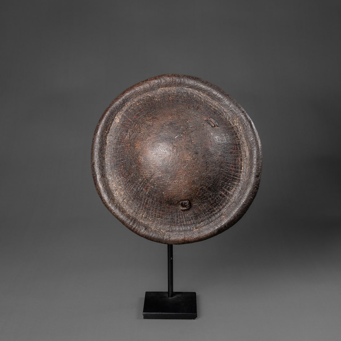 A small Ethiopian shield: Early 20th century, the small round shield made from hippopotamus hide with thick rounded rim, the inside with hide strap handle attached in three places, dark encrusted patina. Dia. 9 ¾ in.,