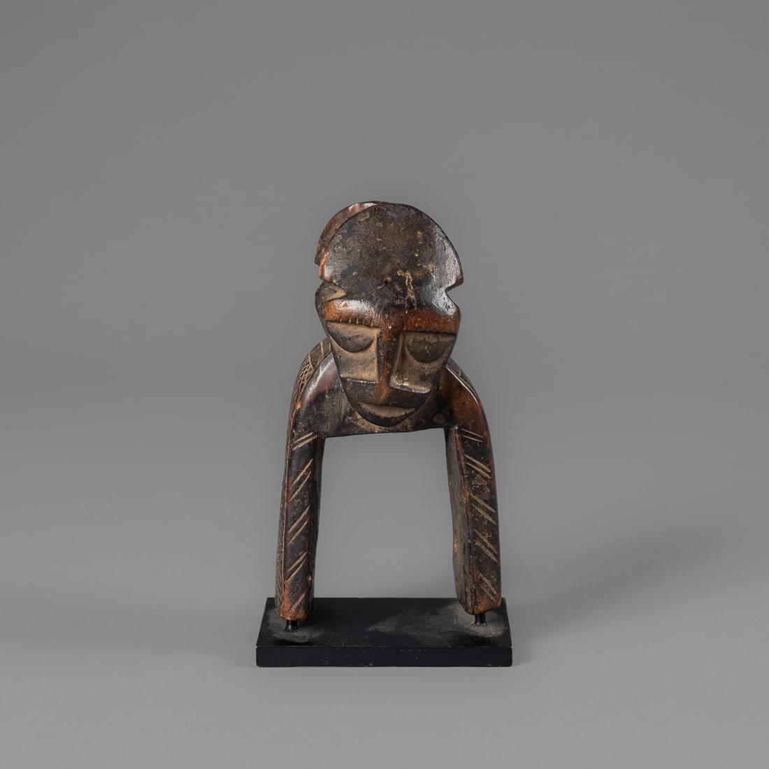 A Djimini heddle pulley: Djimini Peoples, heddle pulley, Cote d’Ivoire, the pulley with chip carved and cross hatched decoration on each side. The two opposing heads joined by central crossbar, mounted on a custom metal sta