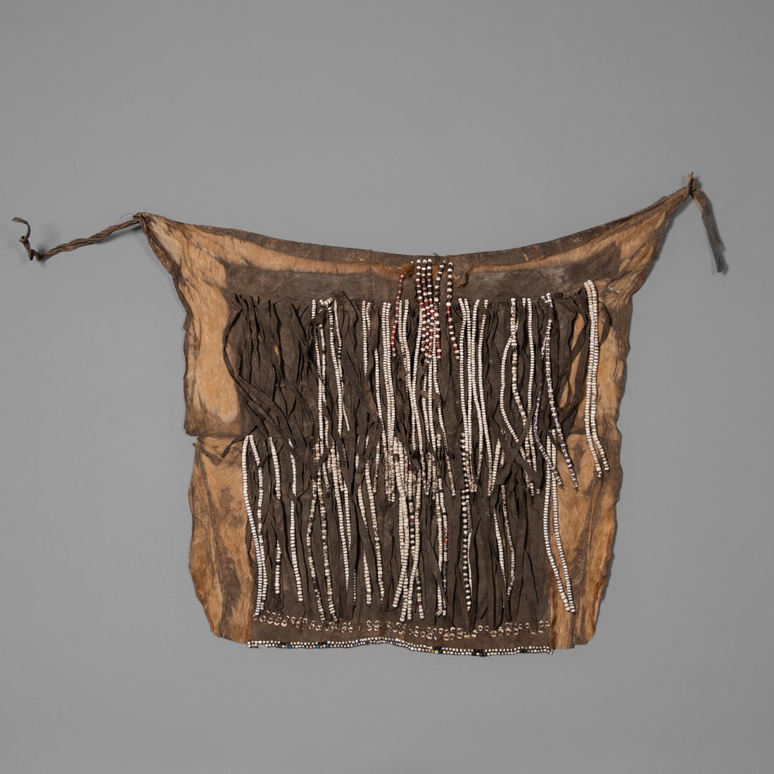 A Mbukushu hide skirt: Botswana, the hide skirt assembled from several hide pieces, the front decorated with black hide fringe and numerous long bead fringes, the bottom with bead edging. Size 21 ½ by 30 in. Provenan