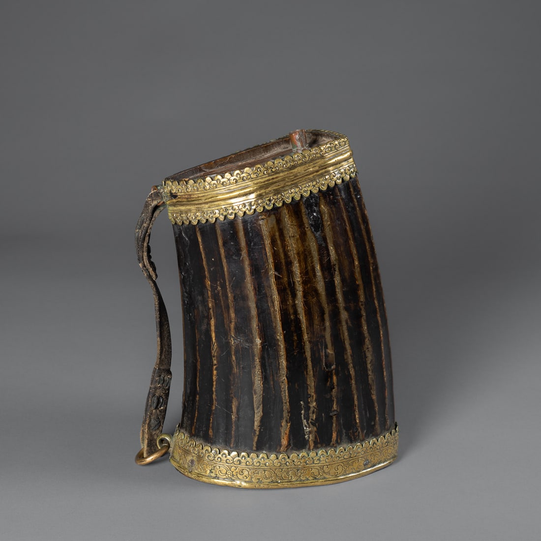 A Tibetan horn and copper beer container: 19th century, the large sheep horn vessel with a heavily tooled brass band around the top and bottom, with hide strap, the top with copper spout, smooth, dark patina. Ht. 10 1/2, wd. 6 1/2 in.