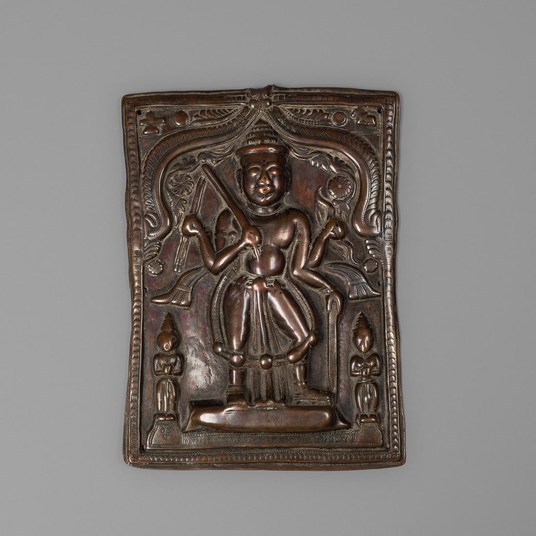 An Indian metal plaque: Maharashtra, late 18th/early 19th century, brass embossed plaque with central figure depicting Virabhadra, standing in an architectural frame, pierced for attachment. Size 8 ¾ by 6 ¼