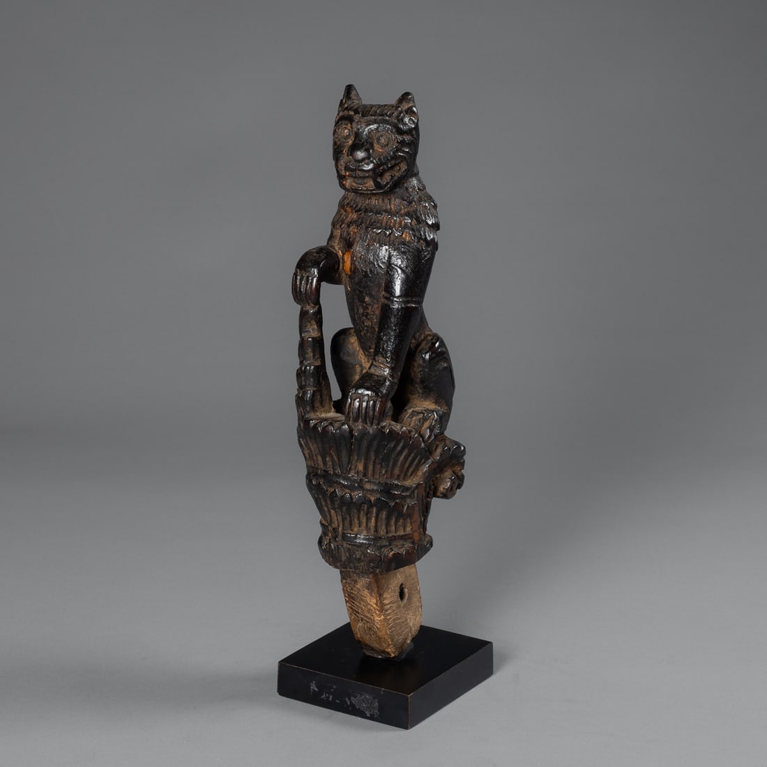 A Burmese ox cart carving: Early 20th century, Chintle ox cart ornament, the standing lion with right paw resting on the projecting ornamental base, smooth dark patina, mounted on a custom base. Ht. 13 in. Provenance: Private