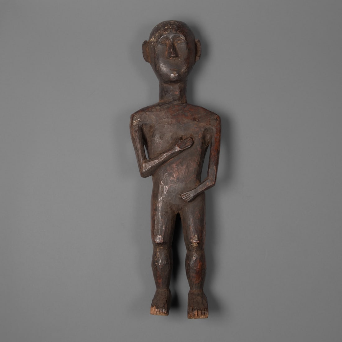 A large Naga wood figure: The carved wooden figure, one hand placed on sternum with the other in front of pelvis, shiny dark patina. Lg. 21 ¾, wd. 6 7/8 in. at shoulder. Provenance: Private collection, Albuquerque, New