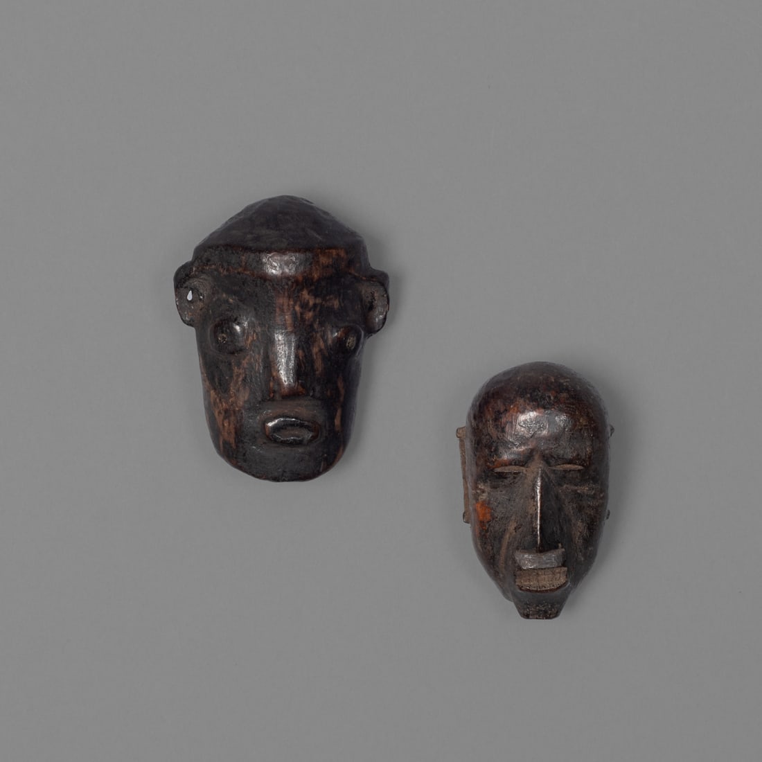 Two Naga wood heads: Konyak, each with rear hollowed out, pierced for suspension, the larger with inlaid eyes, smooth, dark patina. Size 3 x 2 ¼, and 2 ¾ x 1 ½ in. Provenance: Private collection,