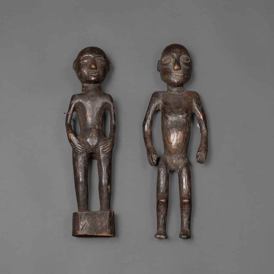 Two Naga wood figures: Konyak, the taller male with arms held wide and pronounced facial features, the female with hands on hips and legs merged with the base, each with smooth, dark patina. Ht. 12 ½ and 12 in.
