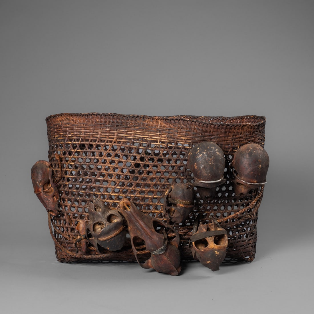 A Naga headhunter basket: The woven basket with two woven baldrics, decorated with eight monkey and rodent skulls tied with original cloth and metal reinforcements. The basket features four different weaving patterns with
