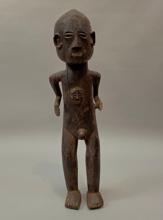 A Naga wood figure: The carved wooden figure, with cut-out arms, a head ornament at the chest, (missing left hand), shiny dark patina. Lg. 17 in. Provenance: Private collection, Albuquerque, New Mexico.