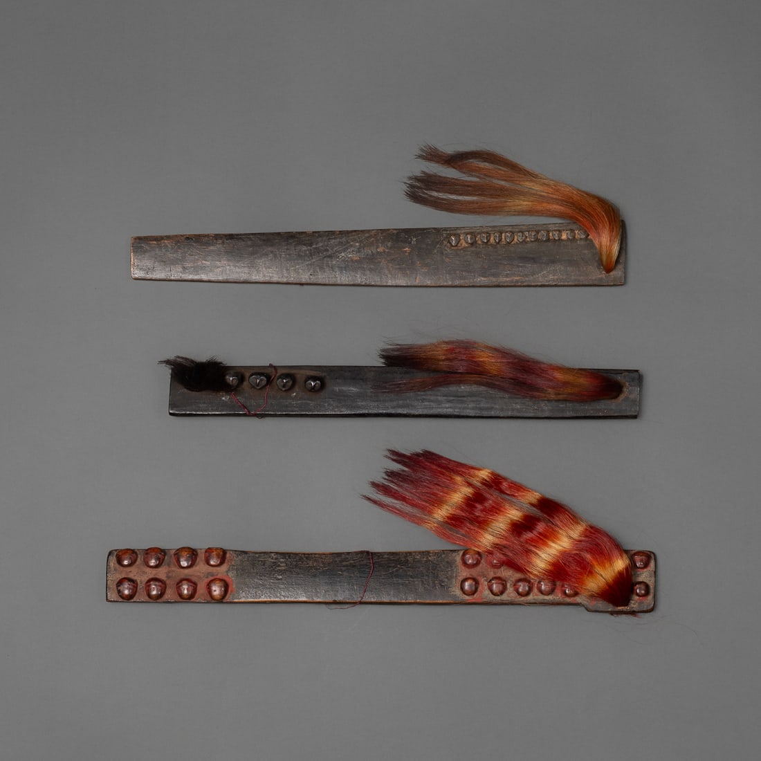 Three wood Naga hairpins: Worn by warriors in a hair knot at back of head, each with rows of raised heads, dyed goat hair tassels, and smooth dark patina. Lg. 12 1/2, 11 ½, 11 in. Provenance: Private collection,