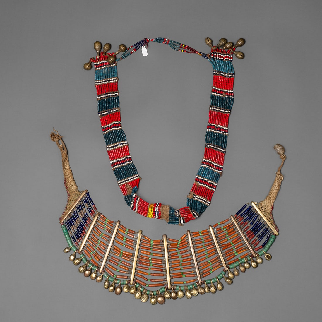 Two bead and brass Naga necklaces: Konyak, the larger necklace with multicolored tubular beads, brass spacers, and brass drops, together with a bead necklace with the ends decorated with brass bells. Lg. 21 ½, 14 ½ in. Pr