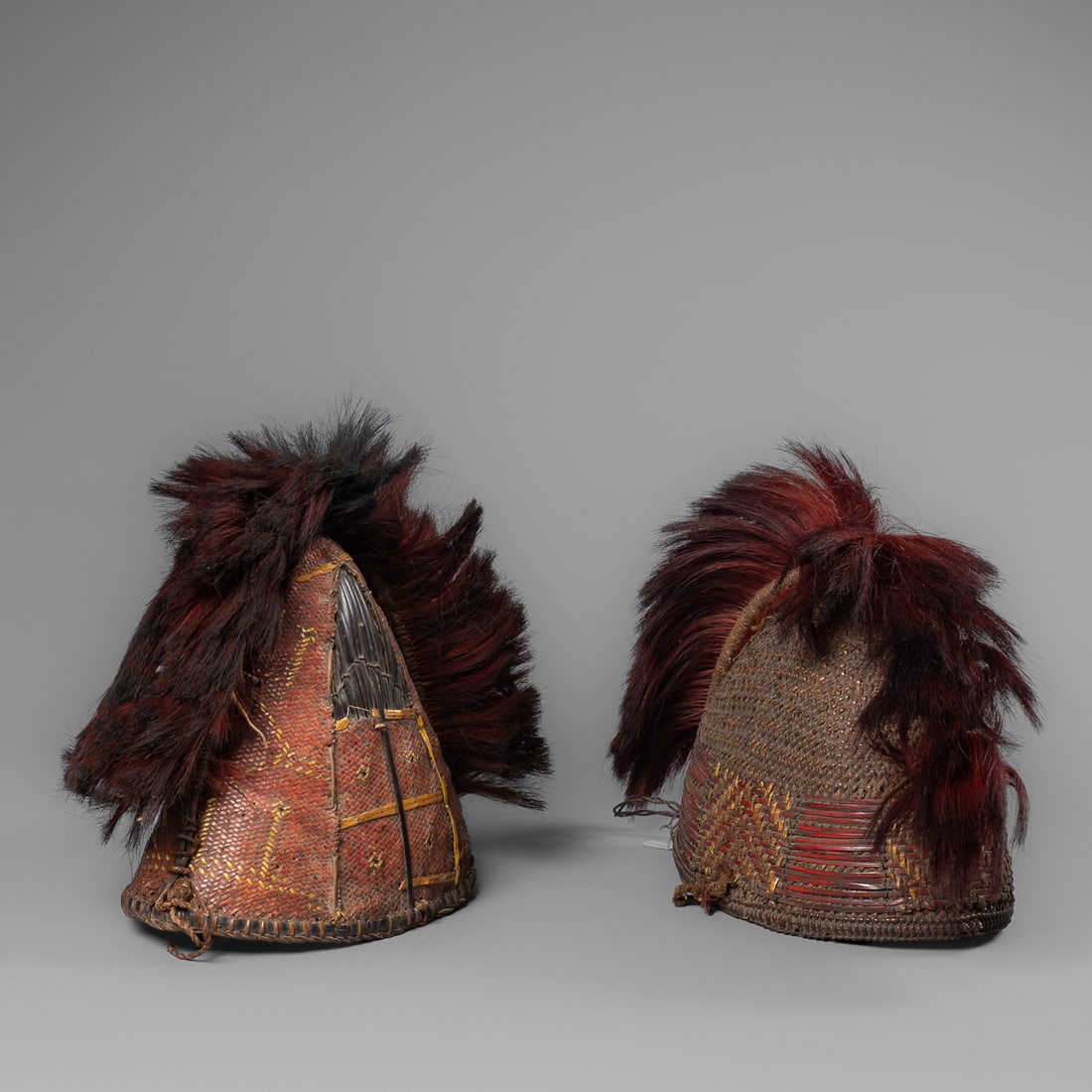Two Naga woven cane hats: Kalyo-Kengyu, two woven cane hats decorated with yellow orchid stem, and dyed goats’ hair. Ht. 9, wd. 11; ht. 9, wd. 11 ½ in. Provenance: Private collection, Albuquerque, New Mexico.