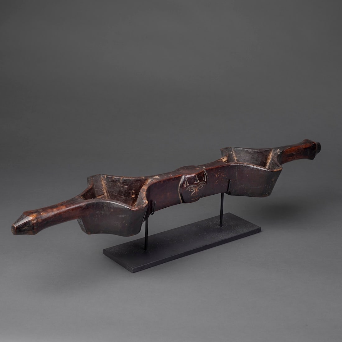 A Paiwan Double Wine Cup, Linnak: 19th century, Taiwan, the two quatrefoil cups on either side of a large face on each side of the vessel, with flaring, square-cut ends, with deep smooth patina, mounted on a metal base, with age
