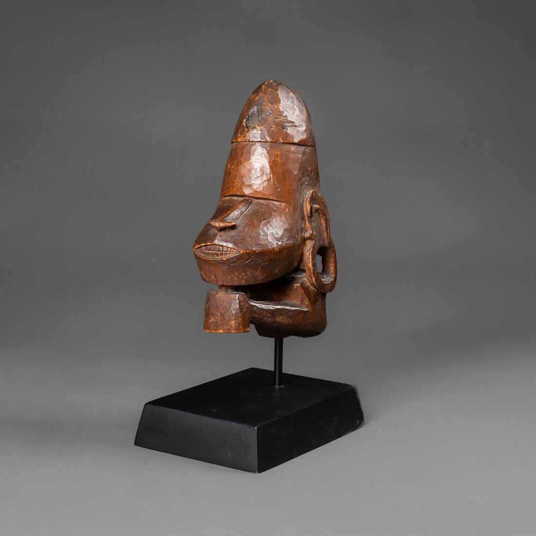 A Solomon Islands canoe prow ornament: Roviana, New Georgia Island, late 19th- early 20th century, the anthropomorphic head with arms raised, hands resting under chin, the open mouth with teeth bared, the elongated face and nose below a