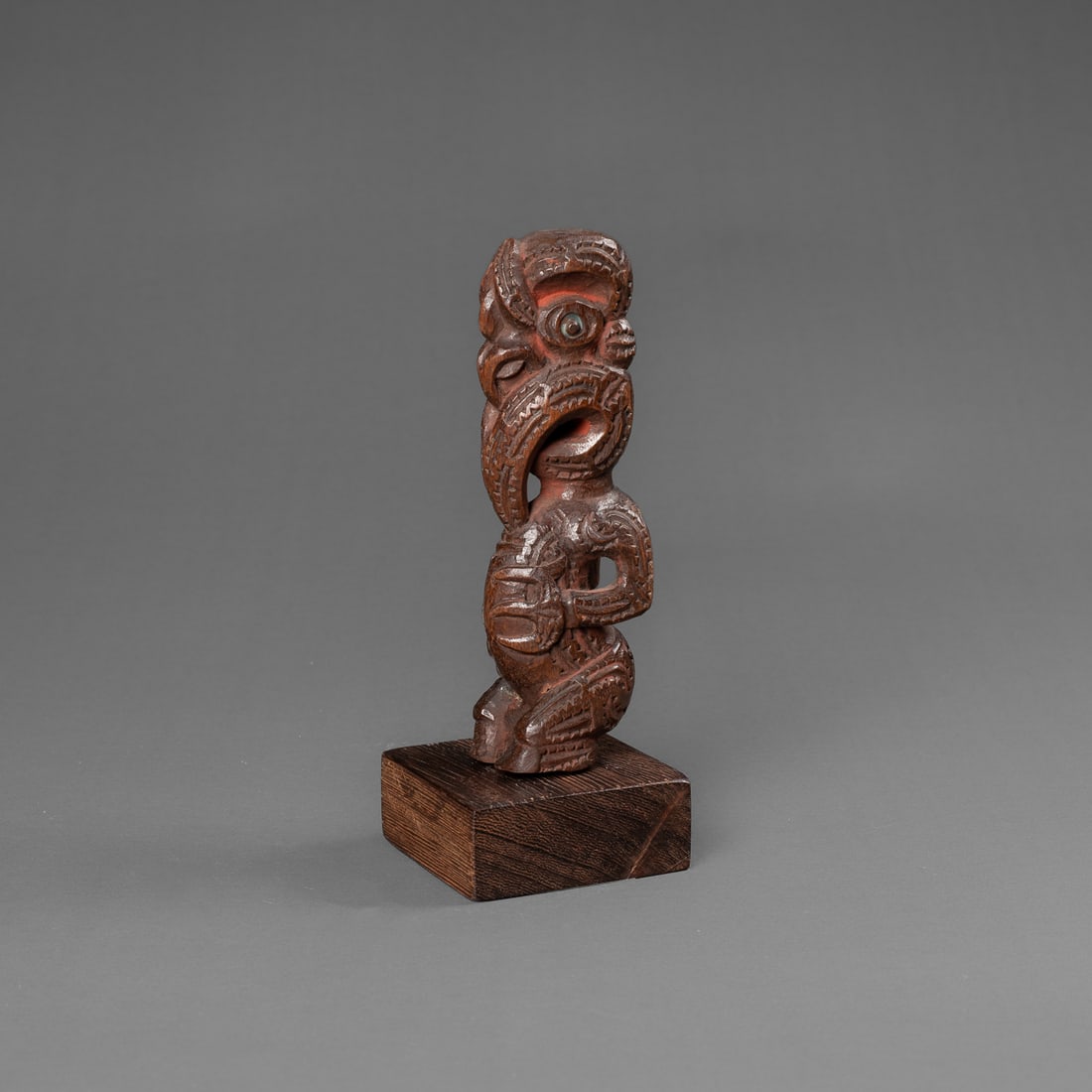 A Maori staff finial: 19th century, the fully carved figure with cut out arms and three fingered hands at stomach, with an abstract face, open mouth, and eyes with paua shell inlay. Probably cut from a ceremonial staff, re