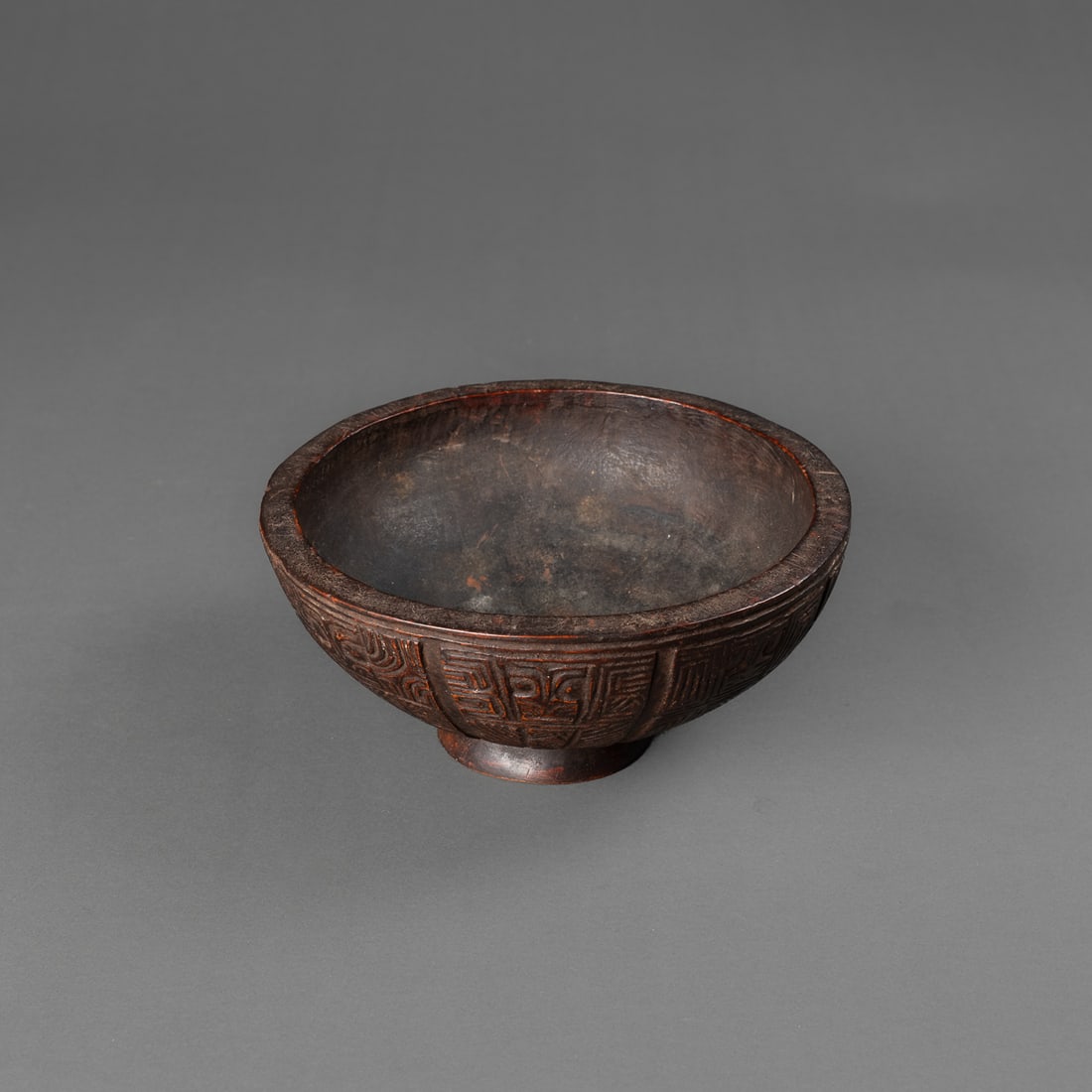 A Marquesan wood bowl: Circa 1880s, the round bowl standing on a small round foot, the exterior fully carved with alternating abstract tiki designs, dark brown patina, Ht. 2 ½, dia. 5 7/8 in. Provenance: Private