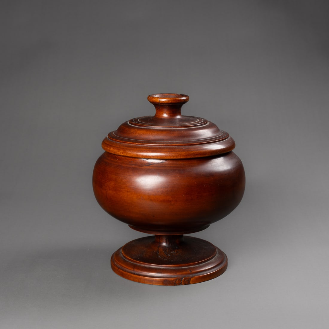 A Hawaiian lidded bowl, umeke: 19th century, monarchy period, the lathe turned bowl with turned lid, part of a large set for luau events, smooth dark brown patina, Ht. 9, wd. 6 ¾ in. Provenance: Private collection, Los Angel