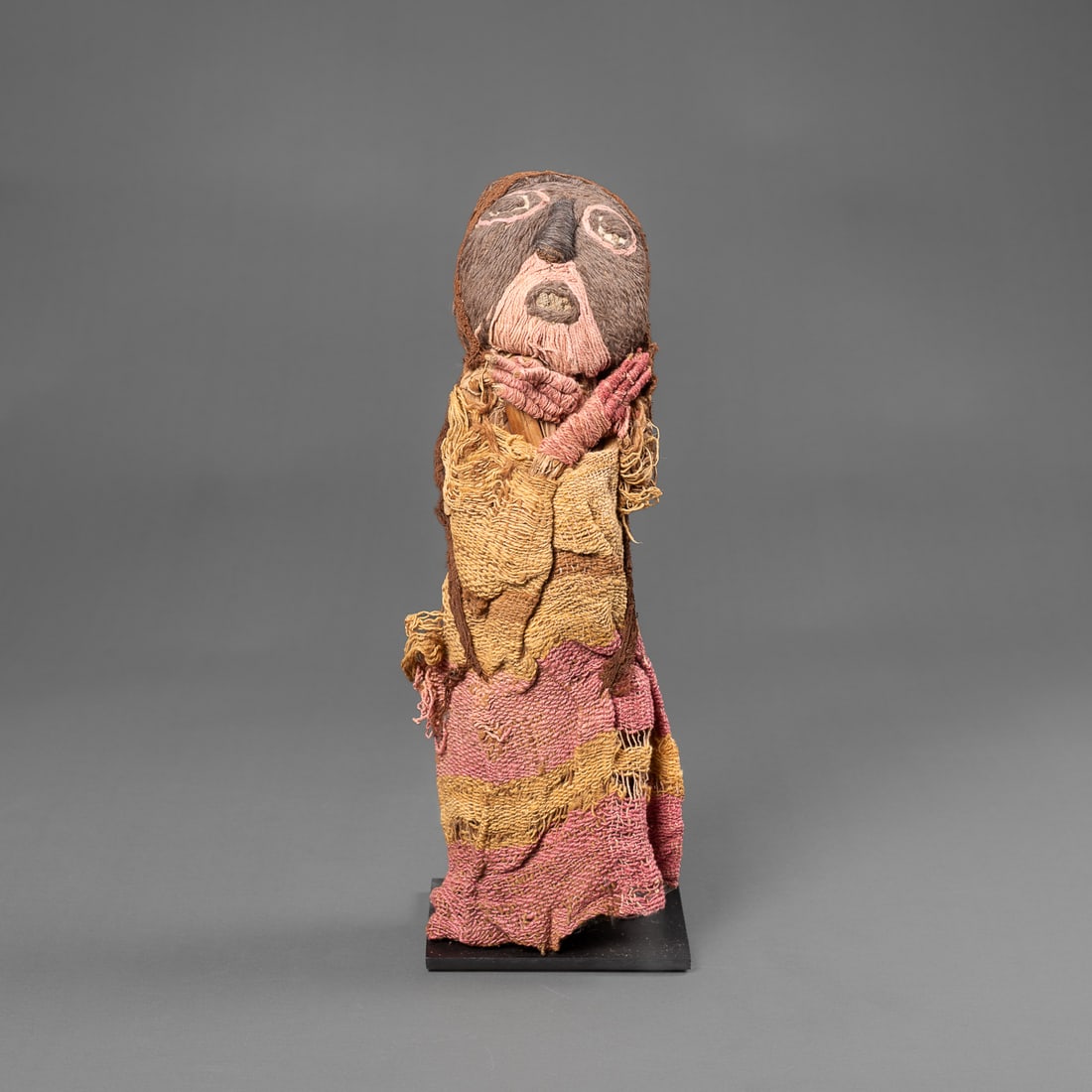 A Pre-Columbian Chancay textile doll: Central coastal Peru, circa 1100-1300 A.D., the camelid wool and fiber textile doll, with pink, brown, and light brown coloring, the female figure with detailed hair and hair covering, the striped clo
