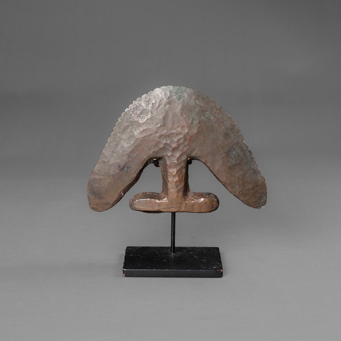 A Pre-Columbian Moche trephination knife: Moche II, Northern Peru, circa 500 A.D., a copper alloy trephination knife, serrated along curved edge, dark smooth patina, with custom stand. Ht. 5 ¾, wd. 5 ½ in. Provenance: Private co