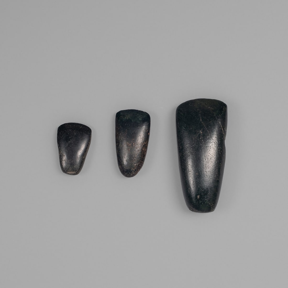 Three Pre-Columbian Mayan celts: Pre-contact, the smooth black stone, with flared, pointed end. The other end, thinner and rounded. Lg. 4, 2 ¼, 1 7/8 in. Provenance: Private collection, Albuquerque, New Mexico; The Foliophiles