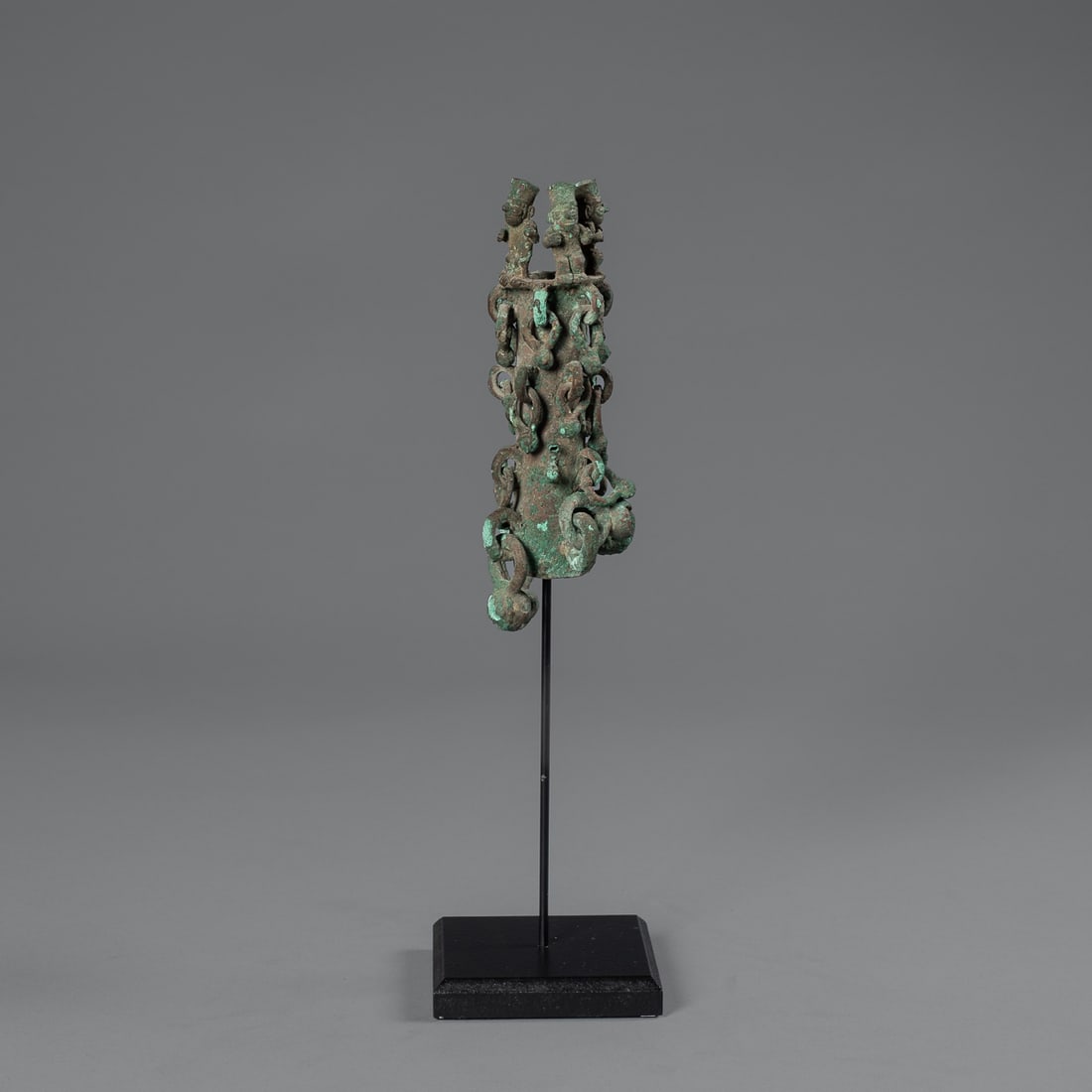 A Moche copper staff finial: Peru, circa 400/600 A.D., the copper finial with numerous loop suspensions below three standing figures at the top, (two figures missing), mounted on a custom stand. Ht. 6 1/4 in. Provenance: Private