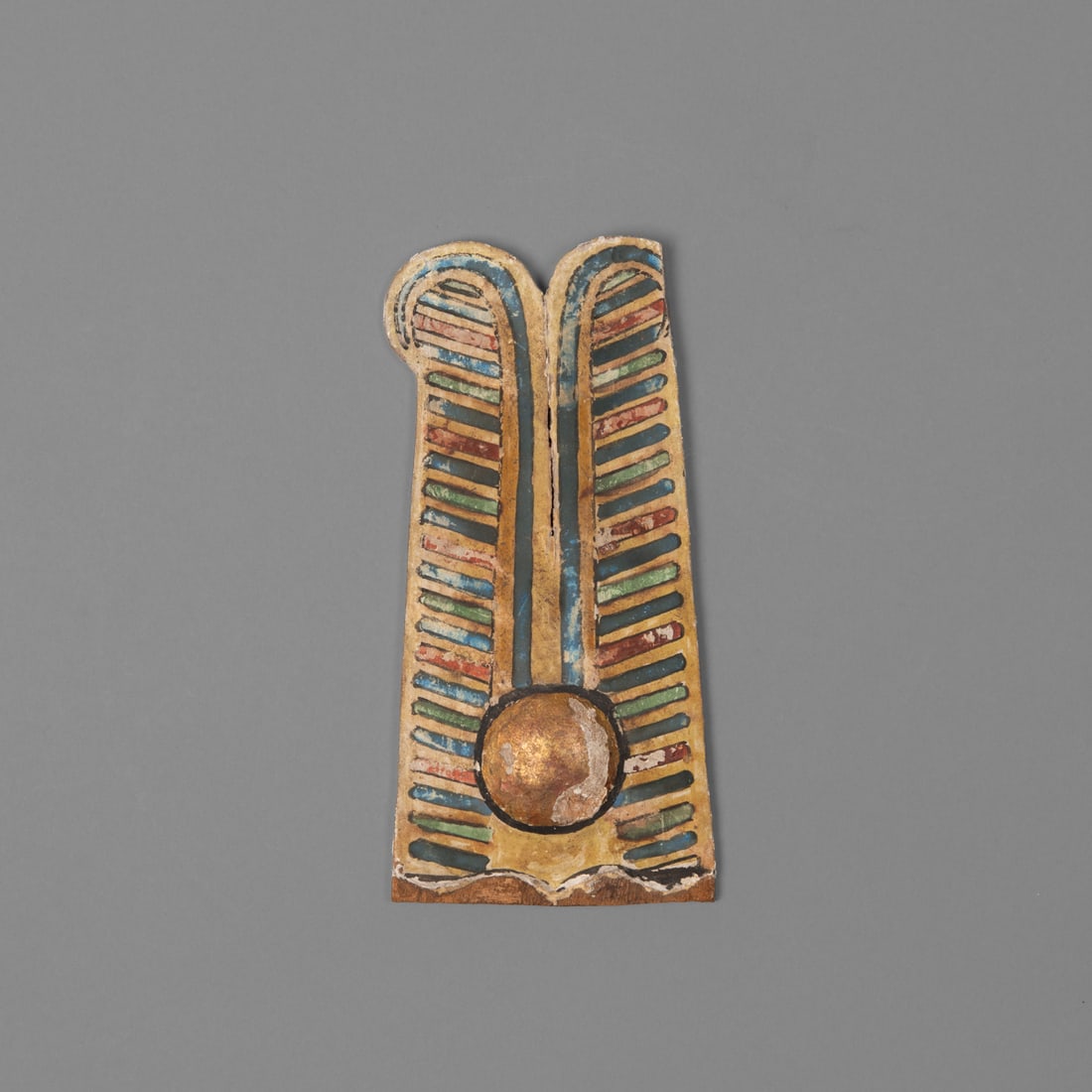 An Egyptian wood Ptah Sokar fragment: Circa 332-30 B.C., the fragment of a headdress from a Ptah-Sokar Osiris figure the central golden circle outlined in black, with two tall plumes with blue, green, and red detailed lines. Provenance: