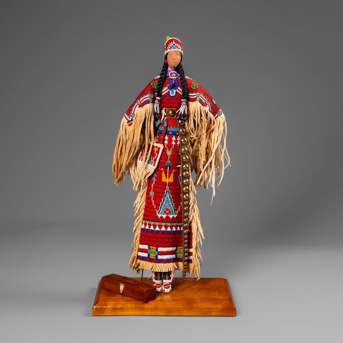 A contemporary Plains doll: Gwen Fedor, Michigan, circa 2000, the standing female doll constructed of wood, wearing a fully beaded hide dress, with hide fringes from the arms, sides, and bottom, with a brass tack belt, beaded