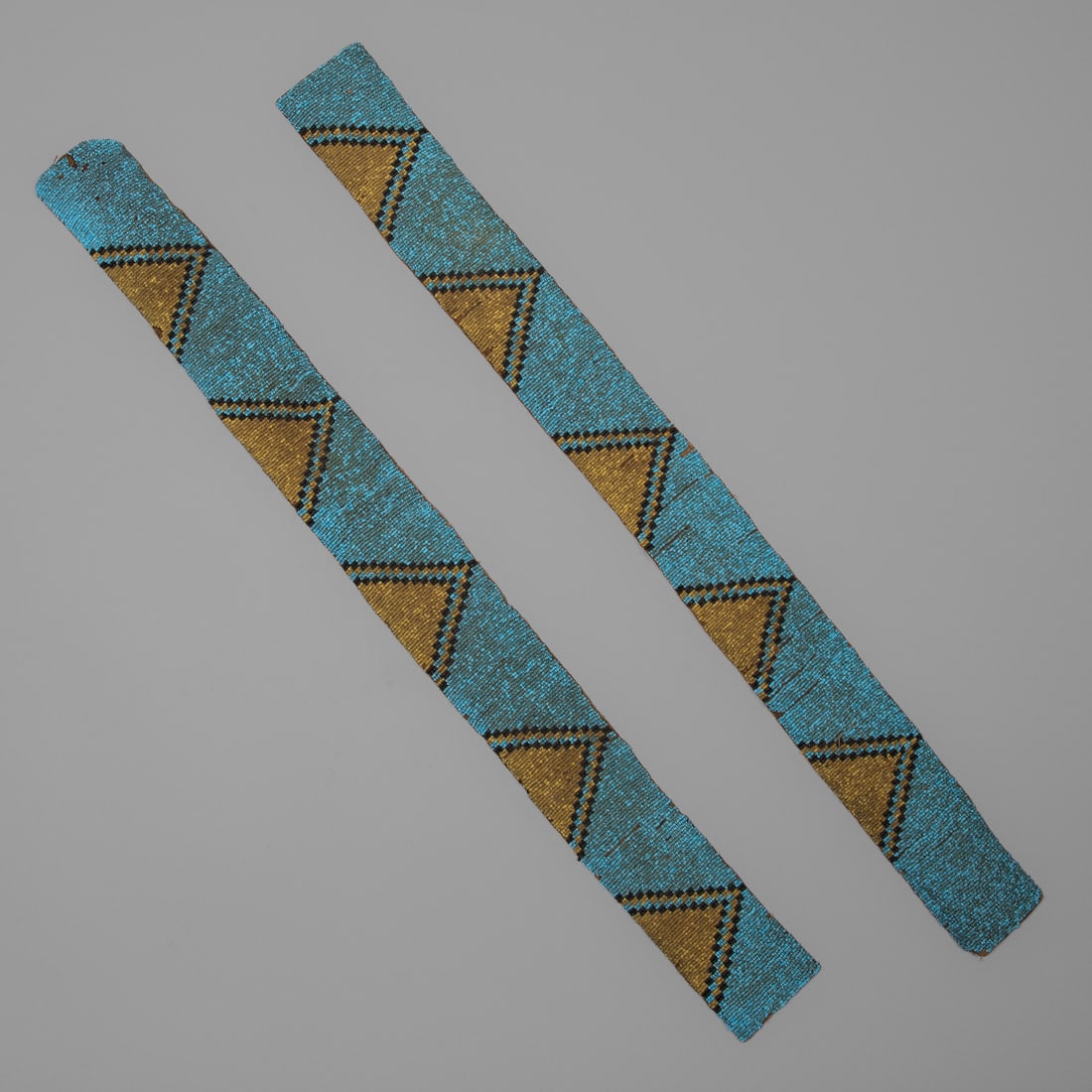 A pair of Plains beaded strips: Fourth quarter 19th century, Lakota beaded strips, beaded on buffalo hide, designed with stepped pyramidal devices on a blue ground. Lg. each 26 3/4, wd. 2 1/2 in. Provenance: Private collection,