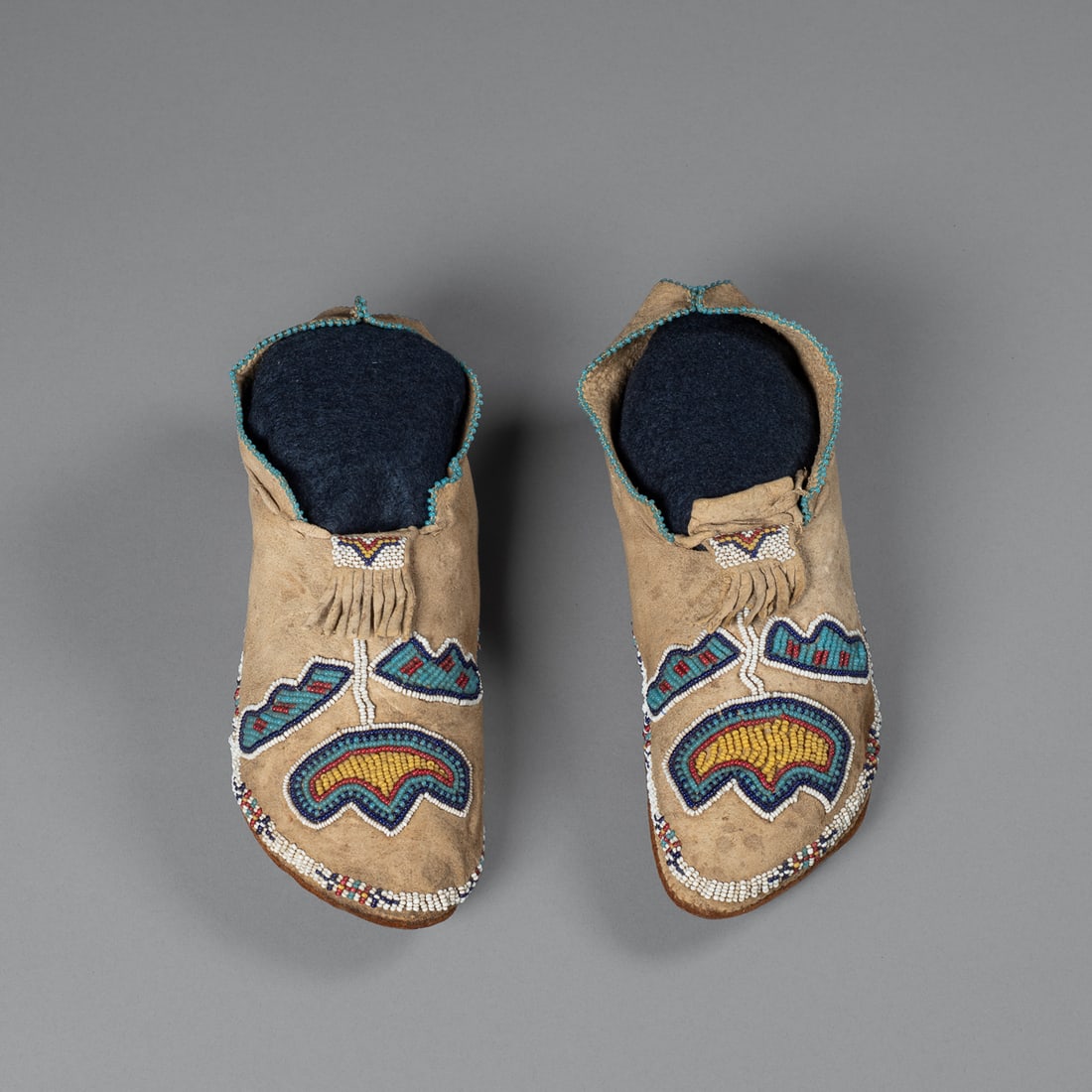 A pair of Kiowa (Southern Plains) child's beaded moccasins: 19th Century, a fine pair of Kiowa children's moccasins featuring commercially tanned leather soles of the type associated with Kiowa dispatch cases and strike-a-lite pouches, Oklahoma, soft-soled