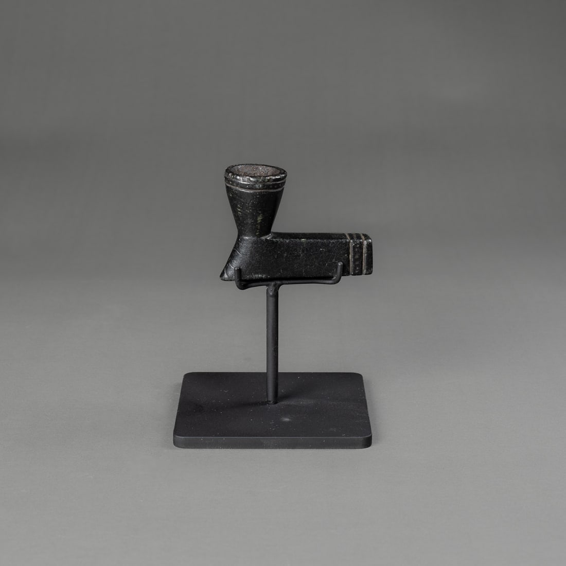 A Chippewa / Ojibwa blackstone pipe bowl: Early 19th century, Chippewa / Ojibwa, the black stone pipe with flared bowl, incised band from rim and two bands from the end. Ht. 2 1/4, lg. 3 1/4 and wd. 1 1/4 in. With metal stand.